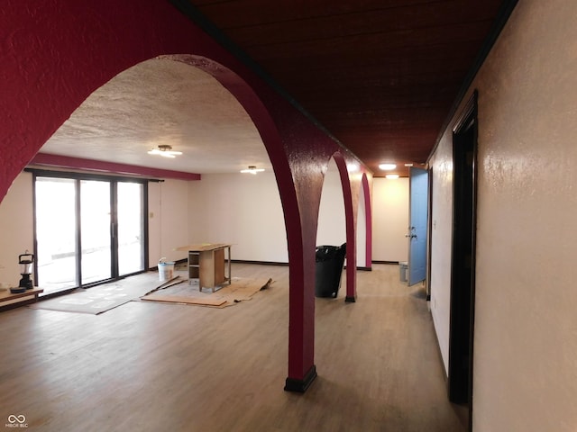 interior space with a textured ceiling, arched walkways, wood finished floors, and a textured wall