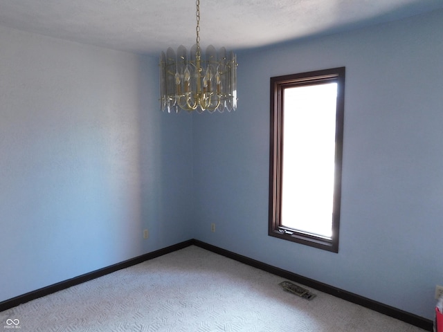 empty room with a chandelier, carpet flooring, visible vents, and baseboards