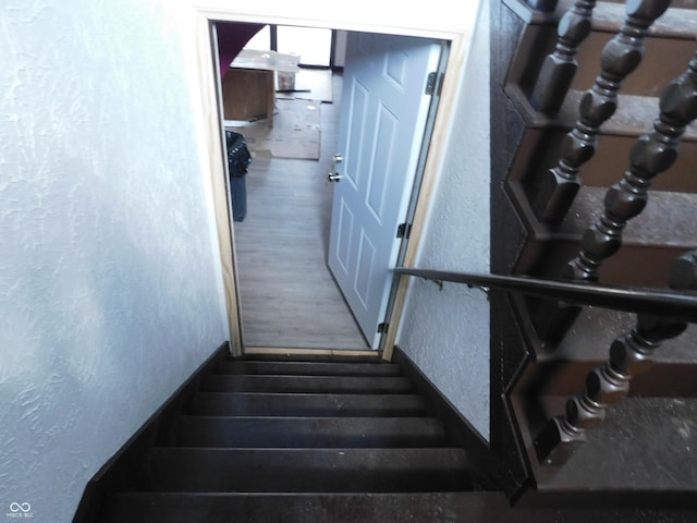 staircase featuring wood finished floors and a textured wall