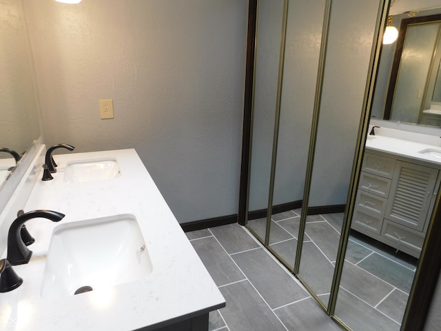 bathroom with a textured wall, tile patterned floors, a sink, and double vanity