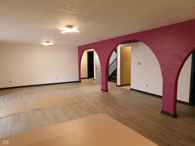 spare room featuring baseboards, arched walkways, stairway, wood finished floors, and a textured ceiling