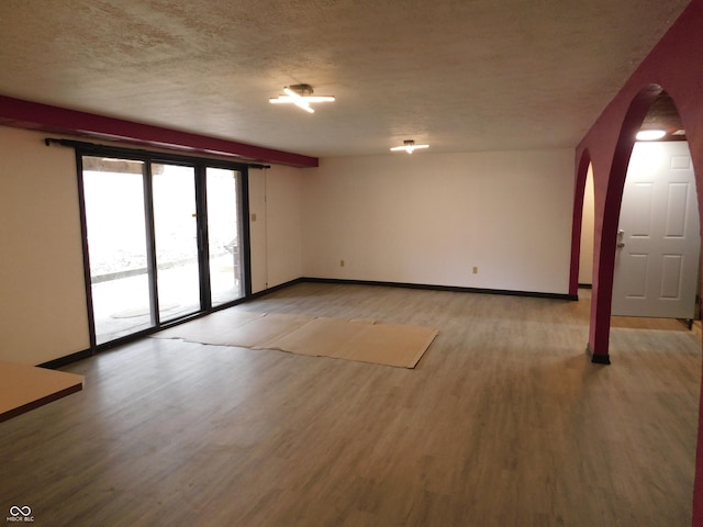 interior space with light wood-style floors, arched walkways, a textured ceiling, and baseboards