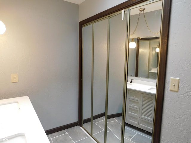 bathroom with a textured wall, tile patterned flooring, vanity, and baseboards