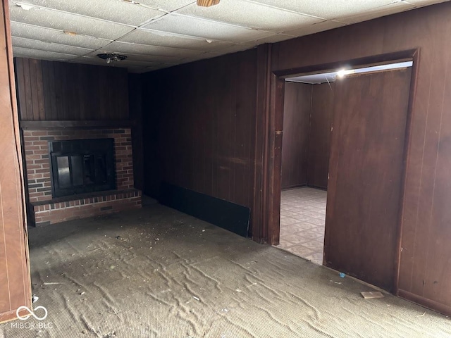 unfurnished living room with a paneled ceiling, a brick fireplace, and wood walls