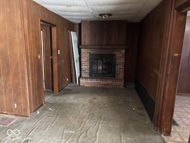 unfurnished living room with a drop ceiling, a fireplace, and wood walls