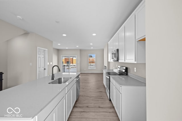 kitchen with appliances with stainless steel finishes, light countertops, light wood-style floors, white cabinetry, and a sink