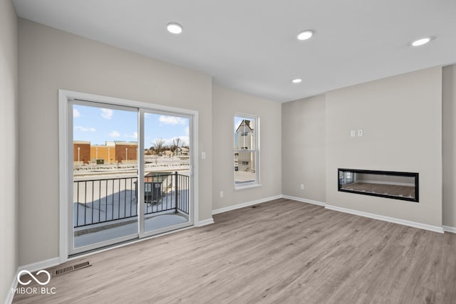 unfurnished living room with wood finished floors, recessed lighting, a glass covered fireplace, and baseboards