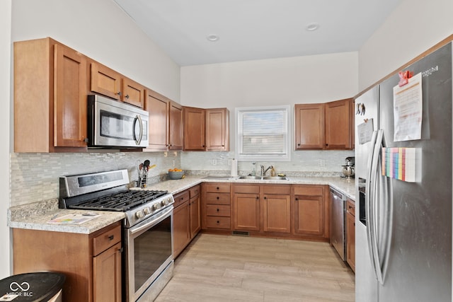 kitchen with light wood-style flooring, a sink, light countertops, appliances with stainless steel finishes, and brown cabinetry