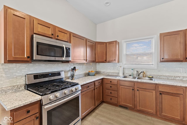 kitchen featuring appliances with stainless steel finishes, brown cabinetry, a sink, and tasteful backsplash