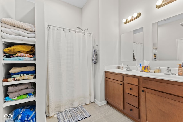 bathroom with wood finished floors, a sink, a shower with shower curtain, and double vanity