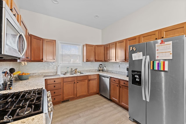 kitchen featuring stainless steel appliances, light wood-type flooring, brown cabinets, and a sink