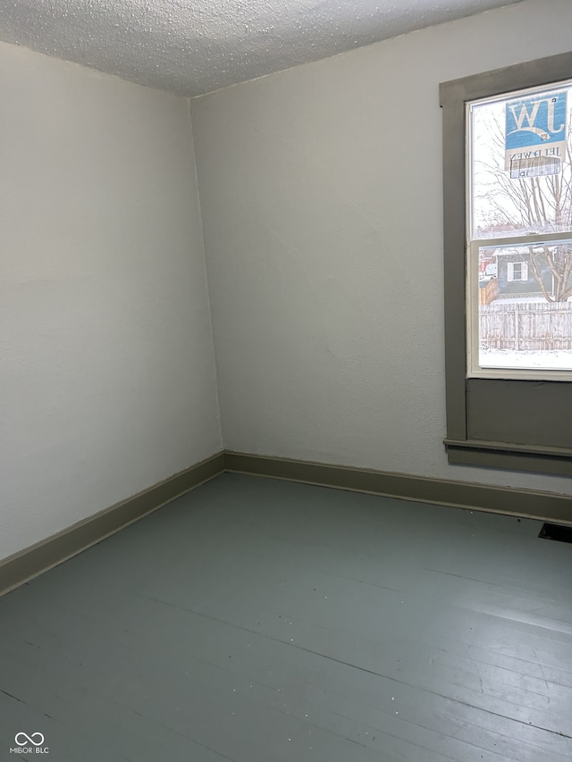 empty room featuring visible vents, a textured ceiling, and baseboards