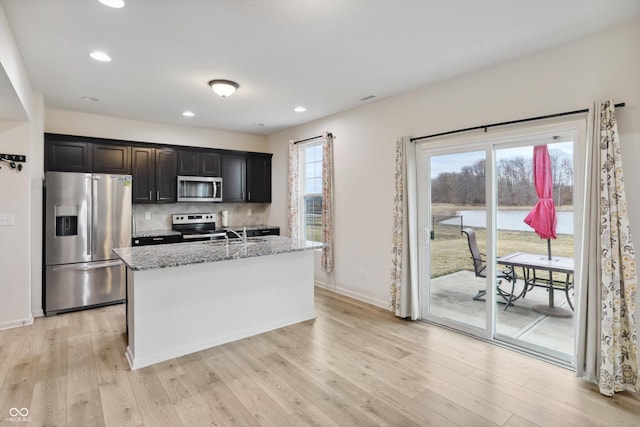 kitchen with baseboards, light stone countertops, stainless steel appliances, light wood-style floors, and backsplash