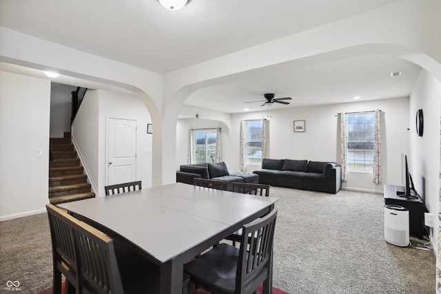 dining room with a ceiling fan, arched walkways, carpet, and stairs