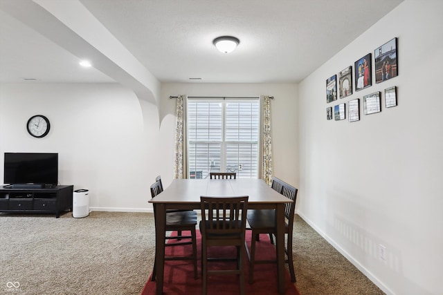 carpeted dining area featuring arched walkways and baseboards