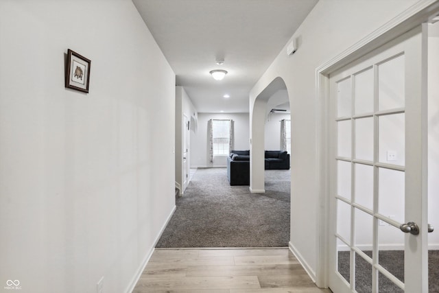 hallway featuring light wood-style floors, arched walkways, light carpet, and baseboards