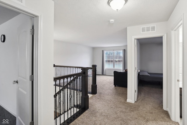 corridor with visible vents, baseboards, carpet, a textured ceiling, and an upstairs landing