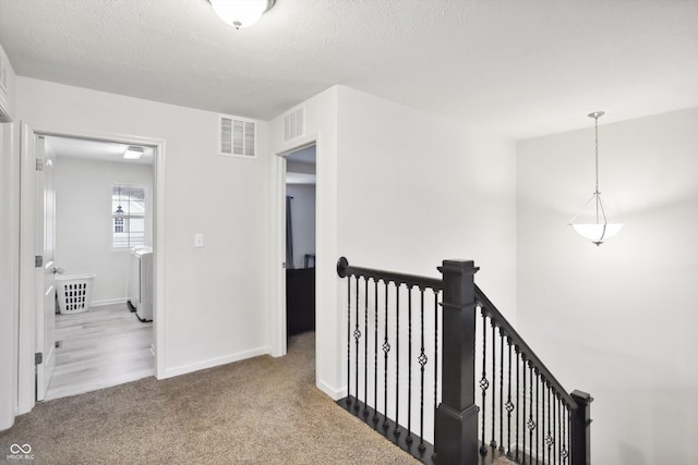 hall with baseboards, visible vents, carpet, a textured ceiling, and an upstairs landing