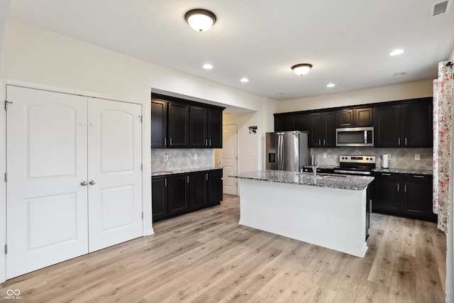 kitchen with stainless steel appliances, stone counters, visible vents, and light wood finished floors