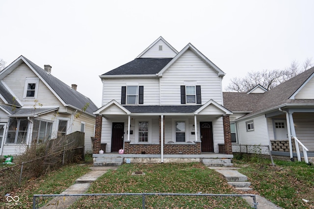 view of front of home featuring a porch, roof with shingles, fence, and brick siding