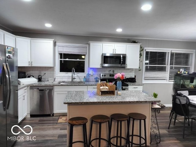 kitchen with dark wood-style floors, a kitchen breakfast bar, stainless steel appliances, white cabinetry, and a sink