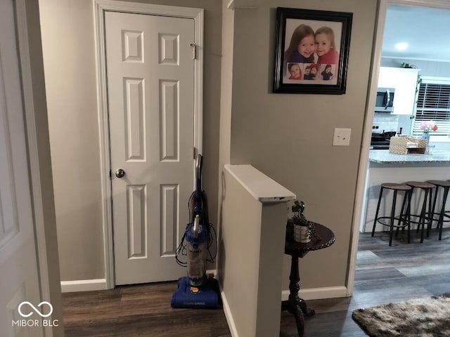 hallway with dark wood finished floors, an upstairs landing, and baseboards