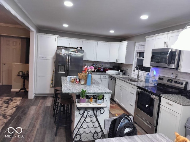 kitchen with light stone counters, a breakfast bar, a sink, white cabinets, and appliances with stainless steel finishes