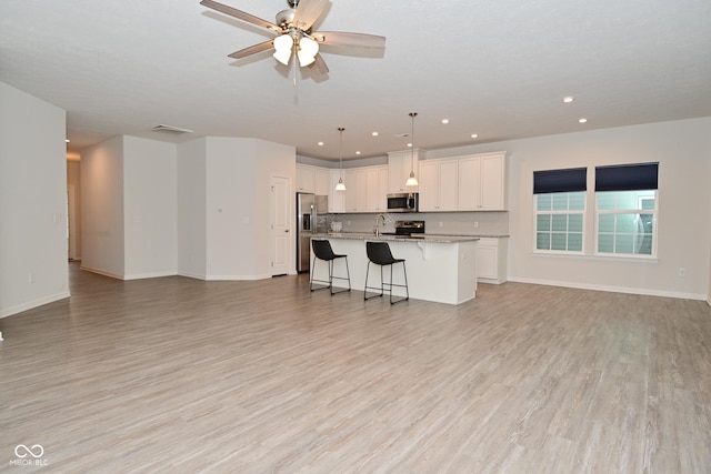 kitchen featuring appliances with stainless steel finishes, open floor plan, light wood-style floors, and a kitchen breakfast bar