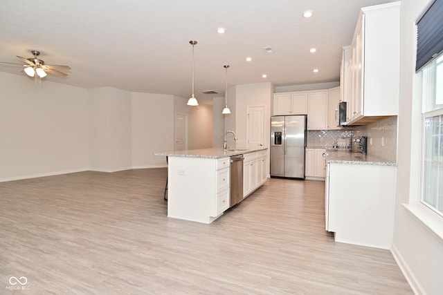 kitchen with stainless steel appliances, decorative backsplash, open floor plan, a kitchen island with sink, and white cabinetry