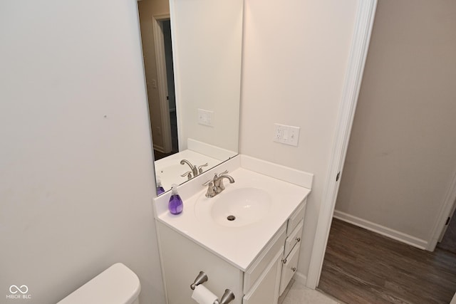 half bath with baseboards, vanity, toilet, and wood finished floors