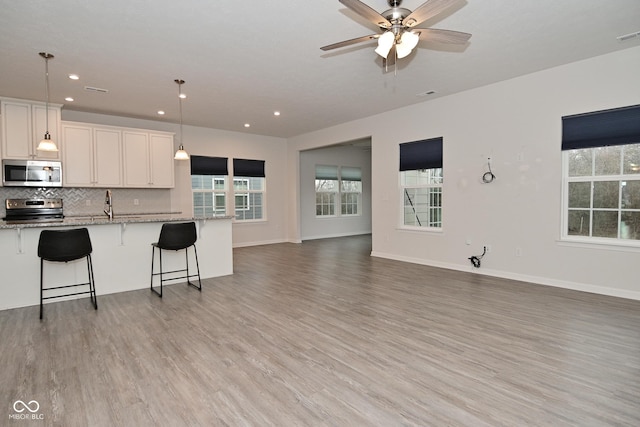 kitchen with open floor plan, appliances with stainless steel finishes, light wood-type flooring, decorative backsplash, and light stone countertops