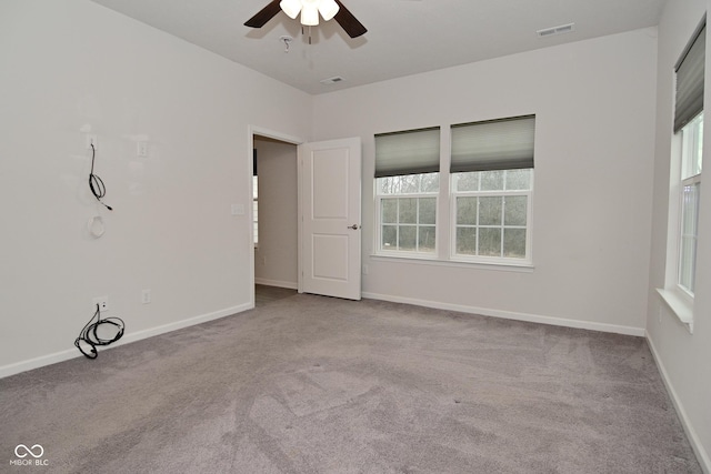 carpeted empty room featuring a ceiling fan, visible vents, and baseboards