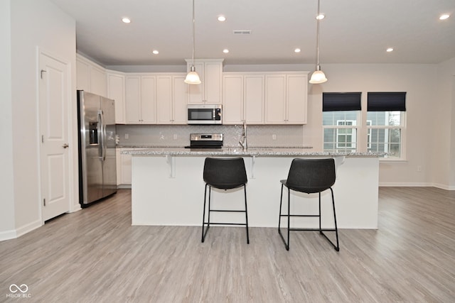 kitchen with light stone countertops, light wood finished floors, tasteful backsplash, and stainless steel appliances