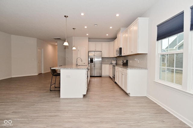 kitchen featuring stainless steel appliances, a breakfast bar, white cabinets, backsplash, and light wood finished floors