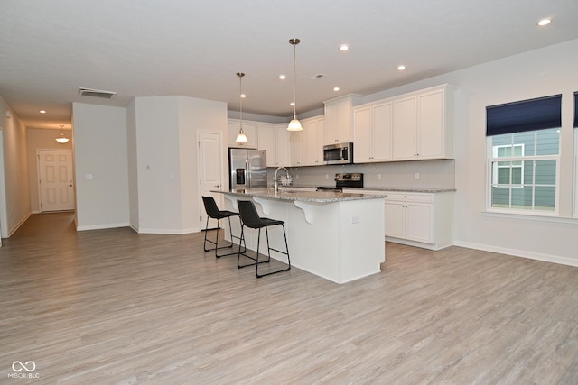 kitchen featuring a breakfast bar area, stainless steel appliances, visible vents, white cabinetry, and a center island with sink