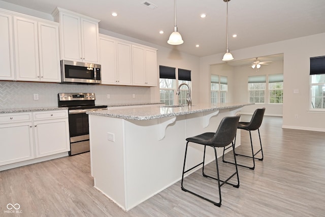 kitchen with tasteful backsplash, visible vents, a kitchen island with sink, stainless steel appliances, and a sink