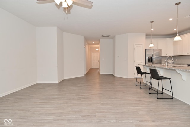 kitchen with a sink, visible vents, a kitchen breakfast bar, stainless steel refrigerator with ice dispenser, and backsplash