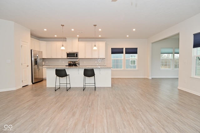 kitchen with tasteful backsplash, light wood-style flooring, appliances with stainless steel finishes, white cabinets, and a kitchen island with sink