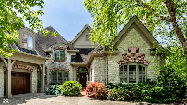 french country inspired facade featuring a garage, stone siding, roof with shingles, and driveway