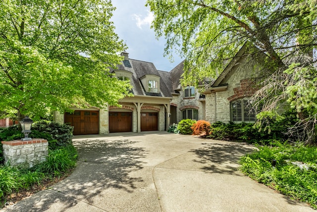 french country home with stone siding, a chimney, and concrete driveway