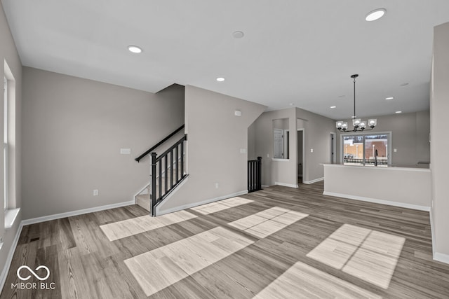 unfurnished living room featuring baseboards, recessed lighting, wood finished floors, and a notable chandelier