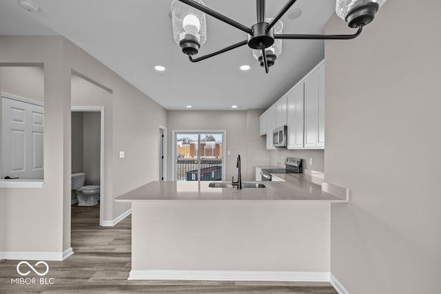 kitchen featuring baseboards, white cabinets, wood finished floors, stainless steel appliances, and a sink