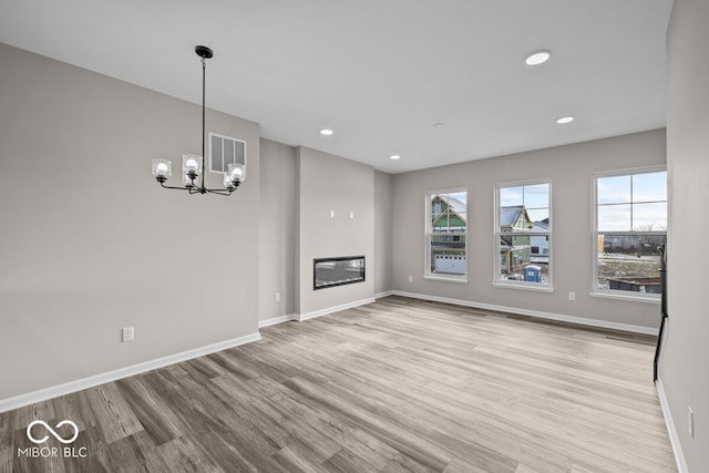 unfurnished living room featuring a chandelier, a glass covered fireplace, baseboards, and wood finished floors