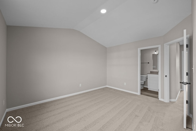 unfurnished bedroom featuring carpet floors, ensuite bath, baseboards, and vaulted ceiling