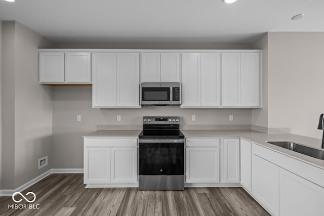 kitchen featuring stainless steel appliances, wood finished floors, a sink, and white cabinets