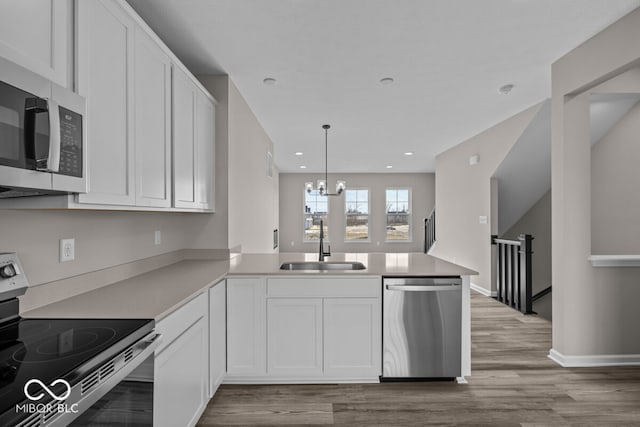 kitchen featuring a peninsula, wood finished floors, a sink, white cabinets, and appliances with stainless steel finishes