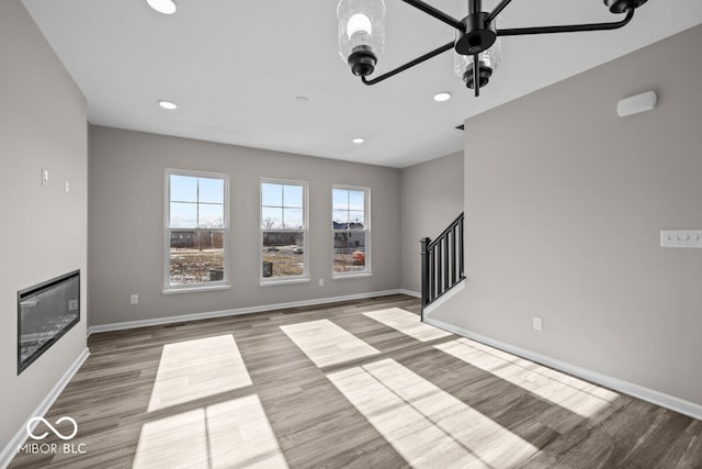 unfurnished living room featuring a glass covered fireplace, stairway, baseboards, and wood finished floors