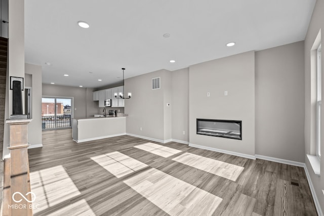 unfurnished living room with visible vents, a glass covered fireplace, wood finished floors, a chandelier, and recessed lighting