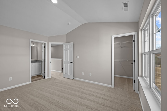 unfurnished bedroom with light colored carpet, visible vents, baseboards, vaulted ceiling, and a spacious closet