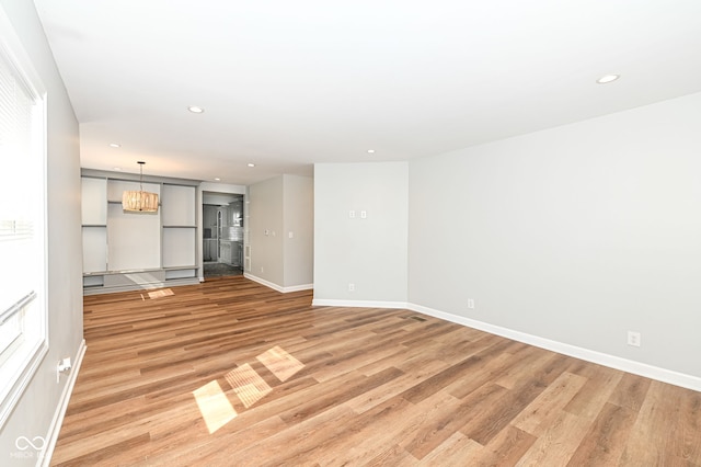 unfurnished living room featuring recessed lighting, an inviting chandelier, light wood-type flooring, and baseboards